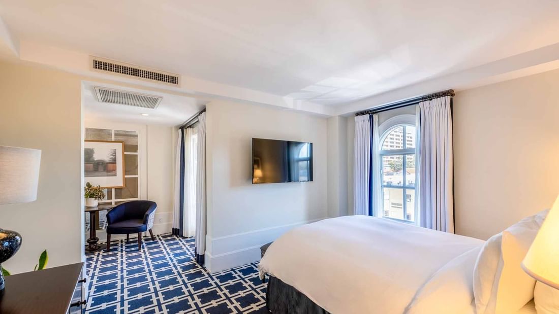 TV and sitting area by the cozy bed in Deluxe Queen Room with carpeted flooring at El Prado Hotel