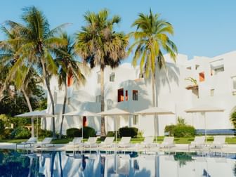 Sunlit tropical Camino Real Zaashila Huatulco with palm trees and poolside lounge chairs under umbrellas