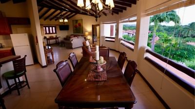 Long wooden dining table under a chandelier with open balcony view in the penthouse at Sugar Cane Club Hotel & Spa