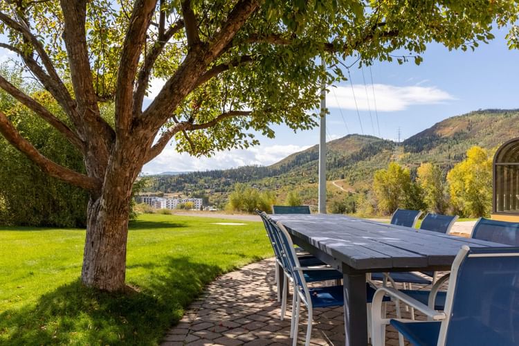 Outdoor dining table with blue chairs under a large tree on green lawn with mountain views at Legacy Vacation Resorts