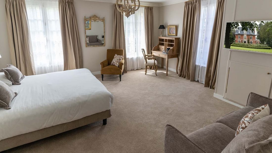 Chambre d'hôtel élégante avec lit, canapé, bureau, chaise, miroir, et télévision murale.