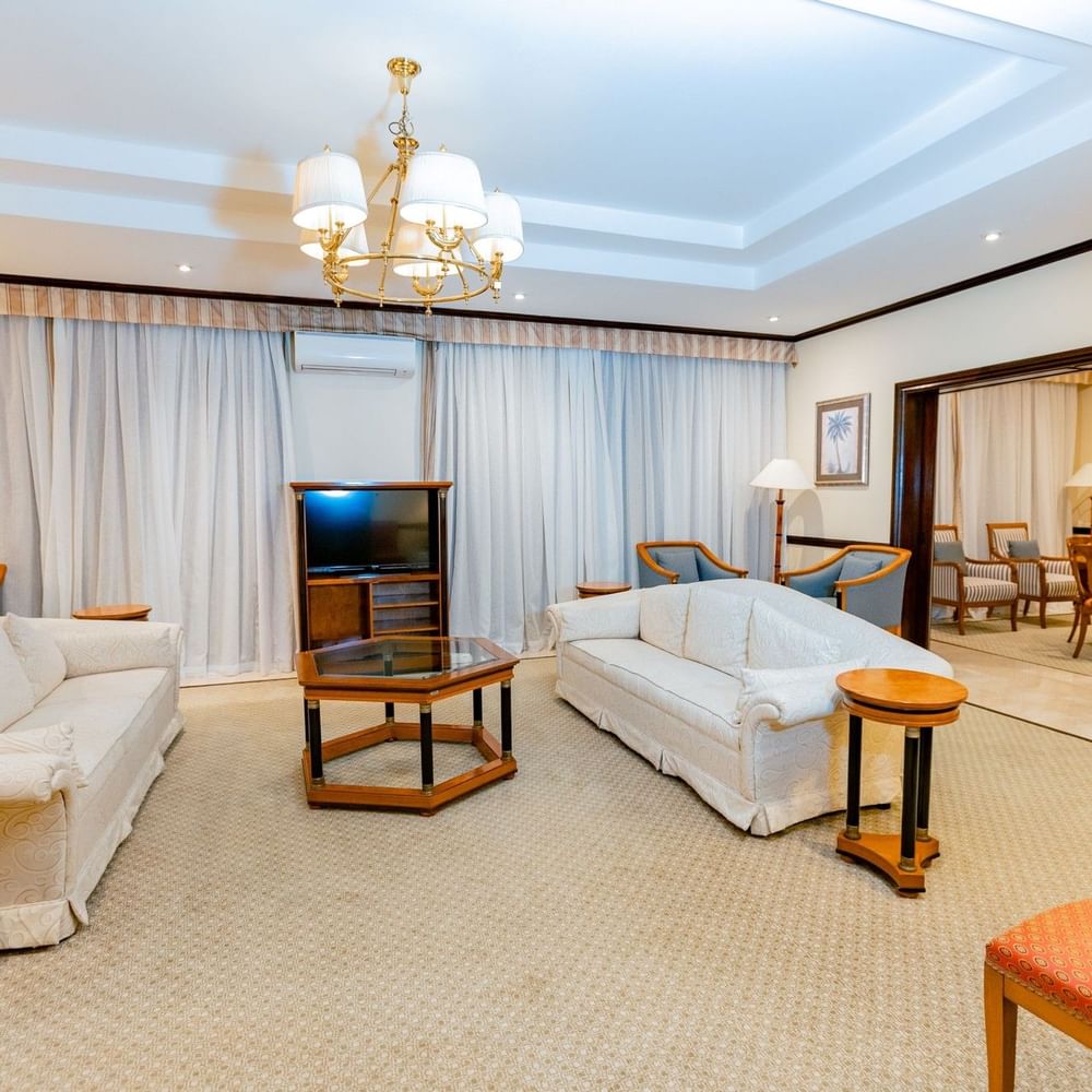 Elegant Presidential Suite living room with white couches, wooden tables, and a chandelier at Dar Es Salaam Serena Hotel.