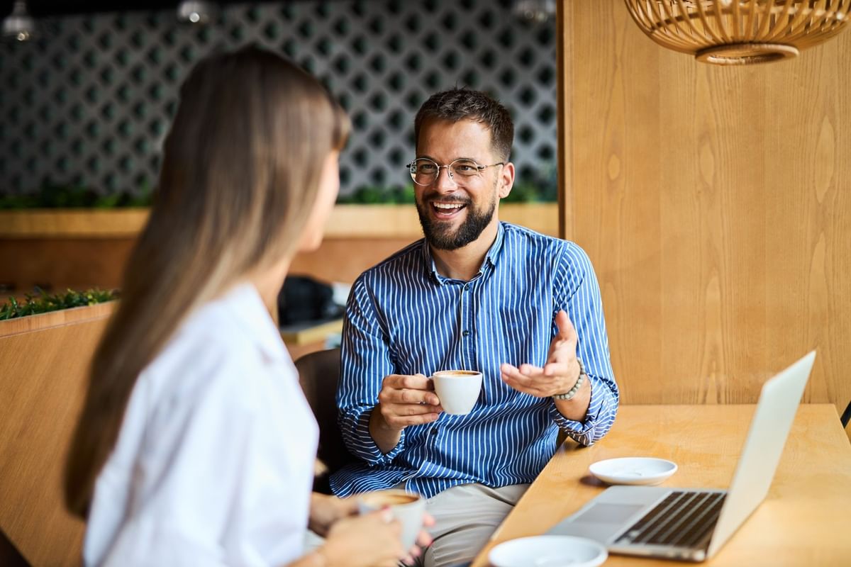 Un hombre alegre con gafas sonríe sosteniendo una taza de café en una reunión en Fiesta Inn