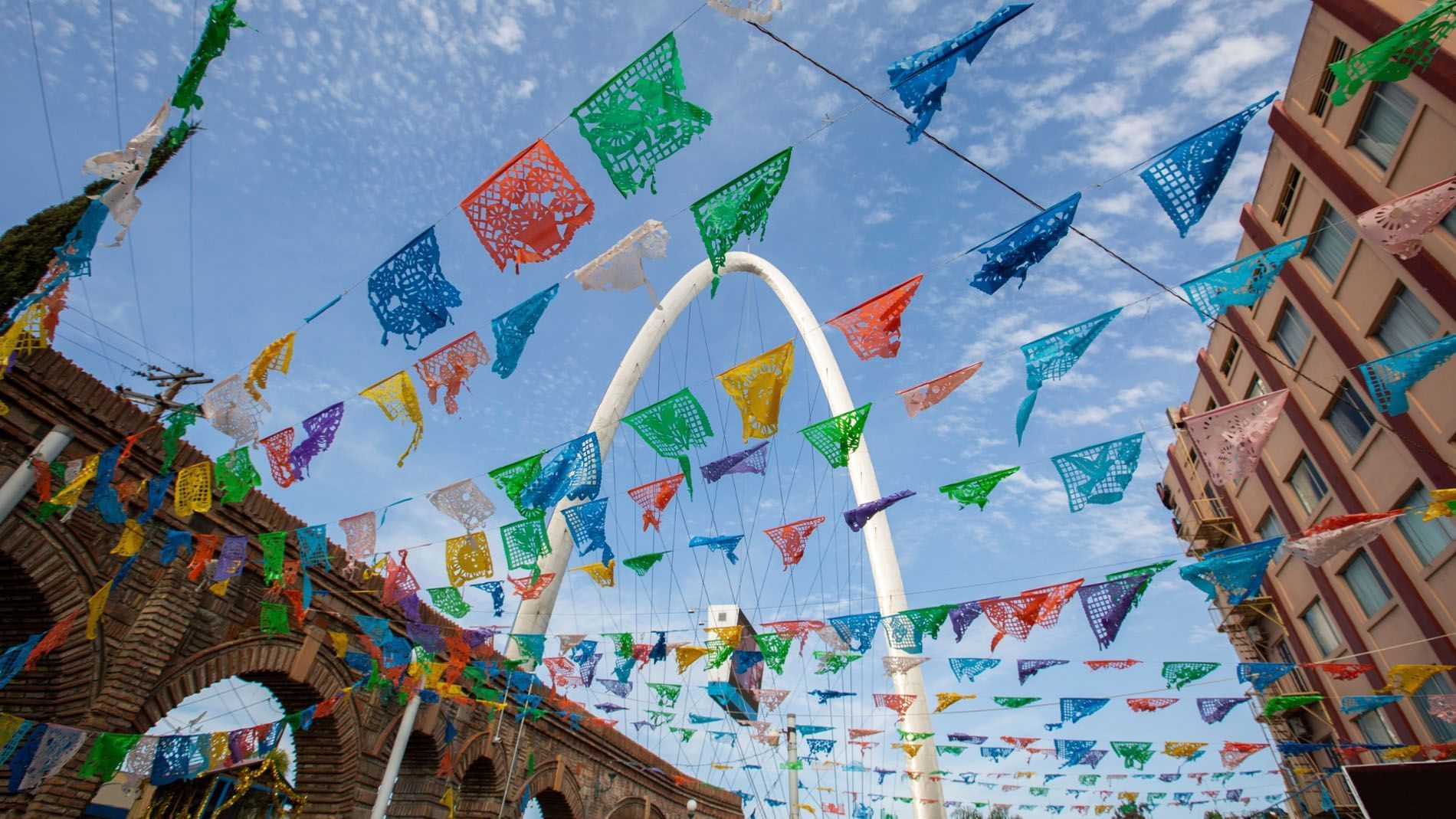 Colorful papel picado banners hang before the Tijuana Arch under a blue sky near the Real Inn Tijuana
