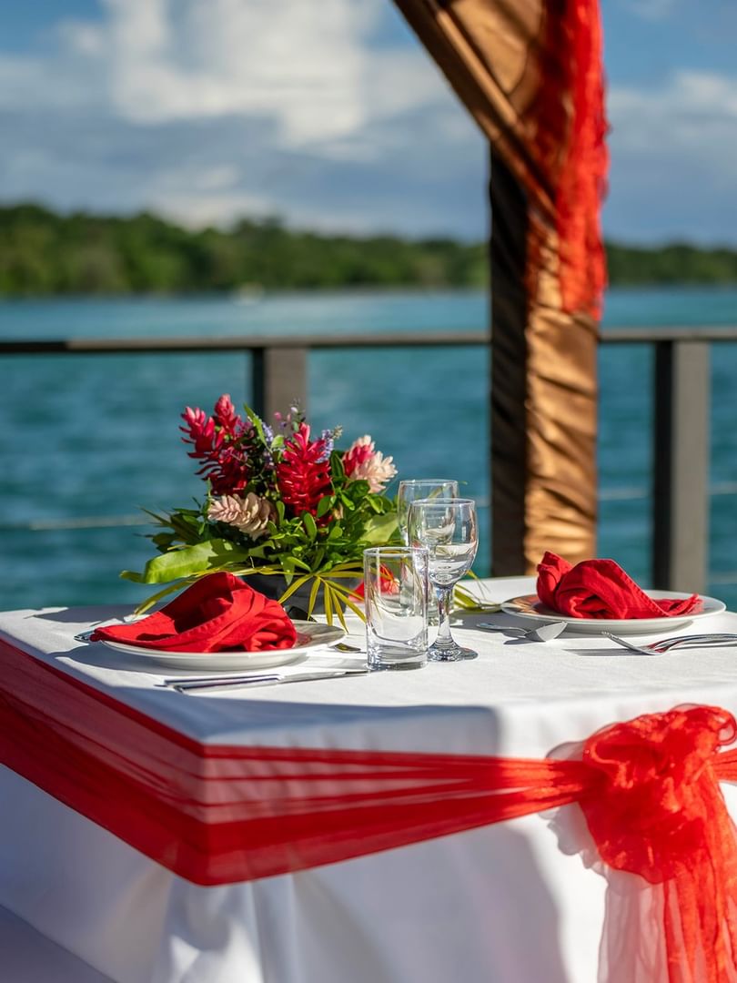 Romantic table by the ocean under a brown canopy featuring red sashes and flowers at Warwick Hotels and Resort