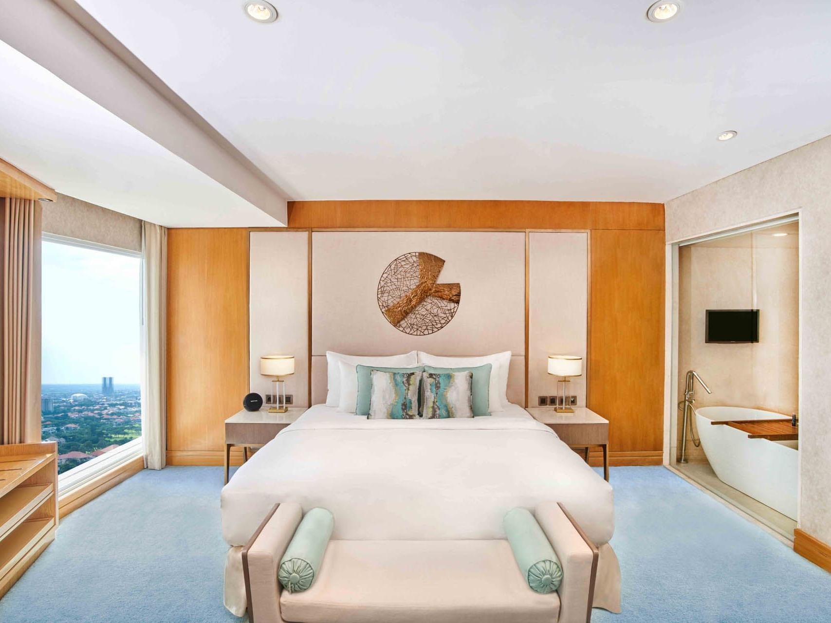 Room with a bed, soft blue carpet, artistic wall decor, and a city view at Vasa Hotel Surabaya