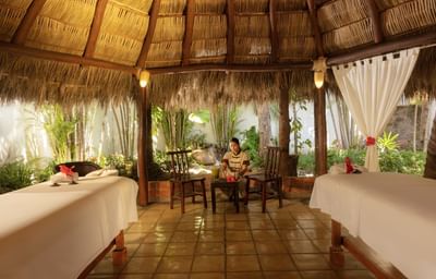 Interior view of a traditional palapa spa relaxation lounge with warm lighting and comfortable seating.