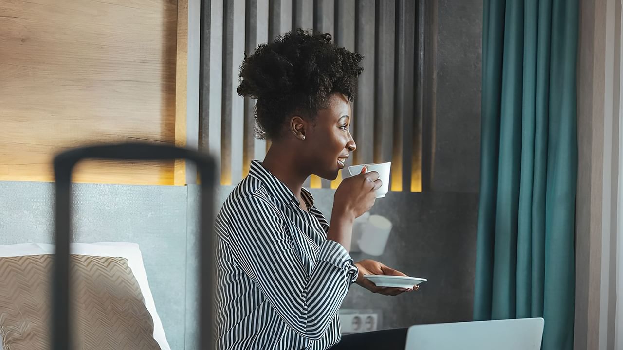 Women drinking coffee on a hotel room bed with laptop open