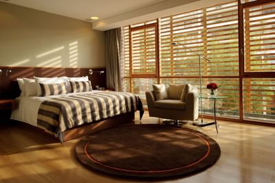 Cama a rayas junto a alfombra redonda en habitaciones Deluxe 2 iluminadas por el sol en NOI Vitacura