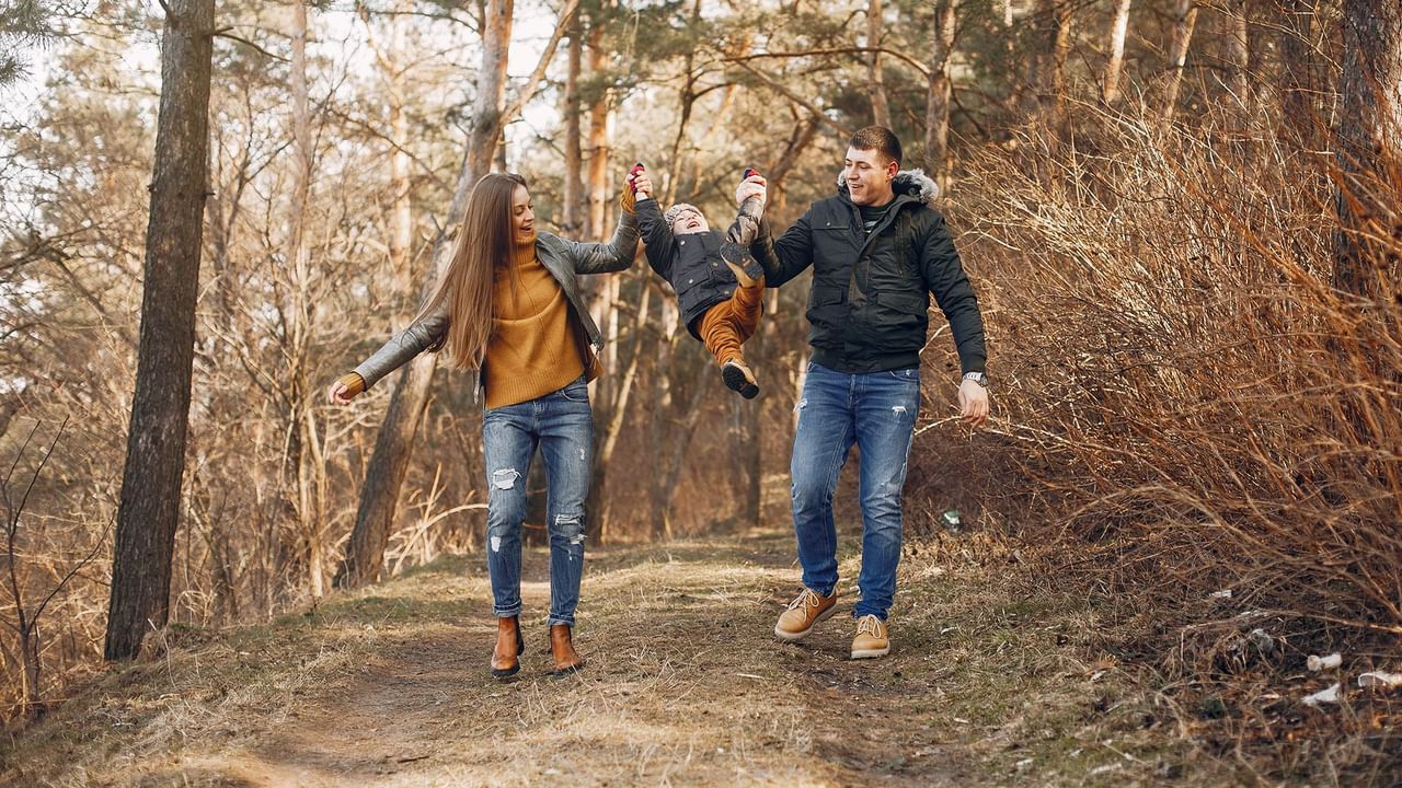 Couple and child in winter attire run on a forest trail, smiling and holding hands.