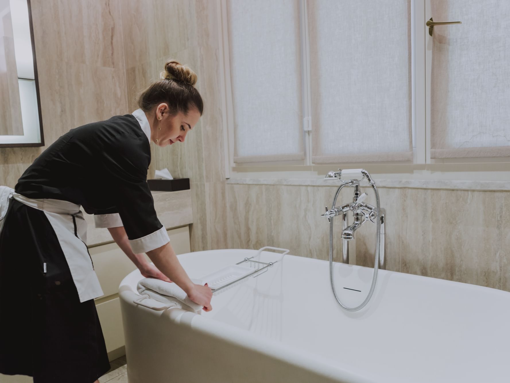 A woman in a black apron diligently cleans a bathtub inside a room at Margutta 19