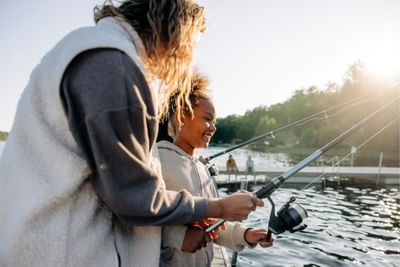 Woman and a young girl are happily fishing from a wooden dock on a lake at sunset near Fall Creek Marina & Campground