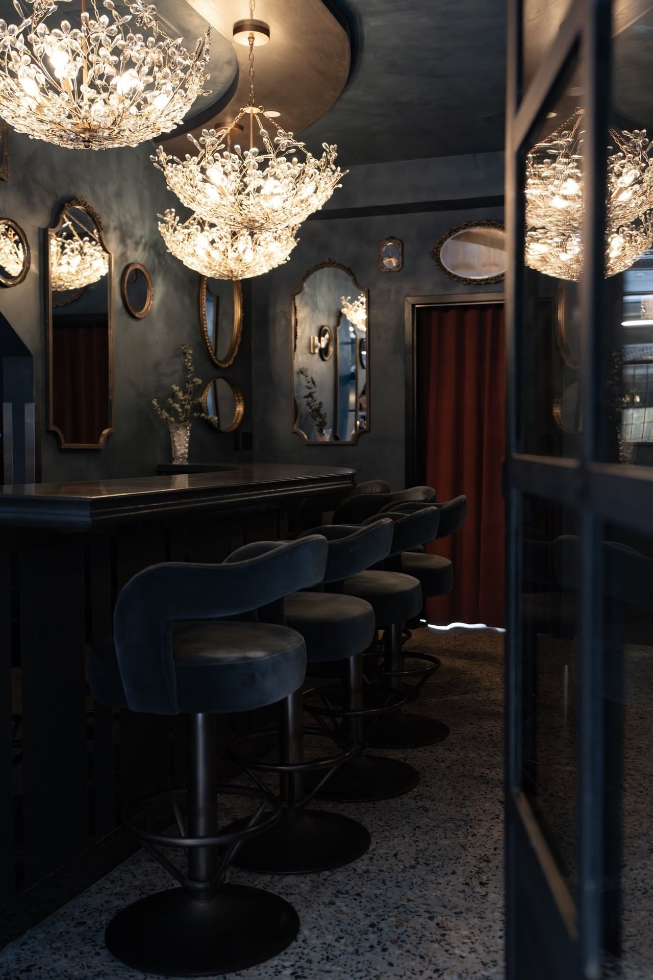 A dimly lit bar with stools, chandeliers, and mirrors on the wall.