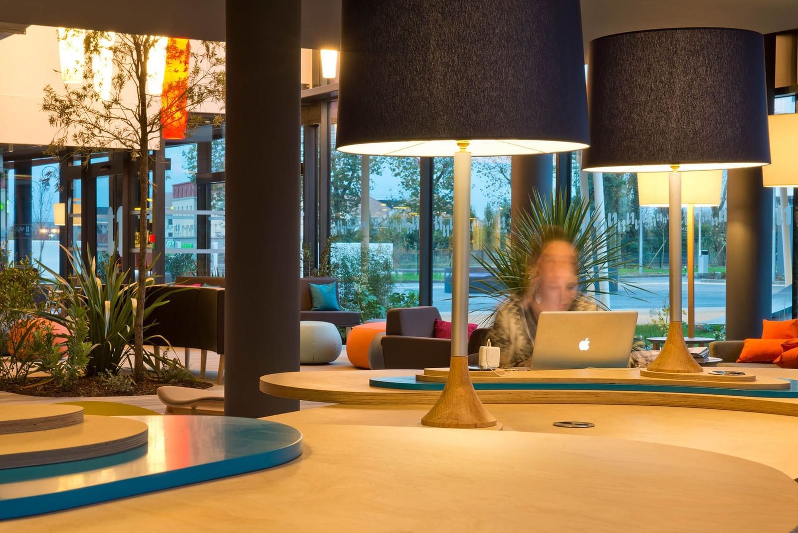 A woman sitting at a desk in a Business Corner at Nomad Hotels Paris Roissy