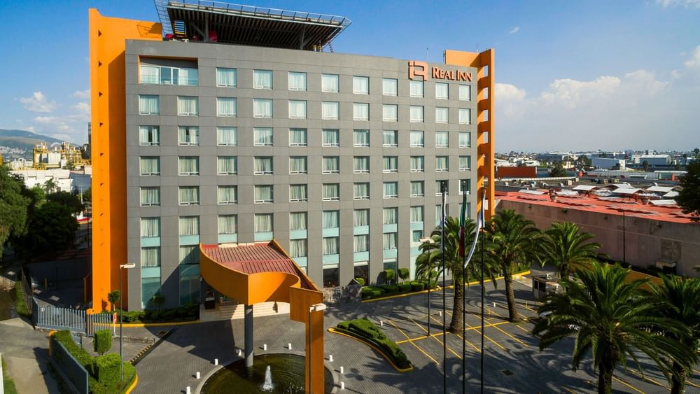 Exterior of Real Inn Perinorte building featuring gray and orange accents and palm tree parking