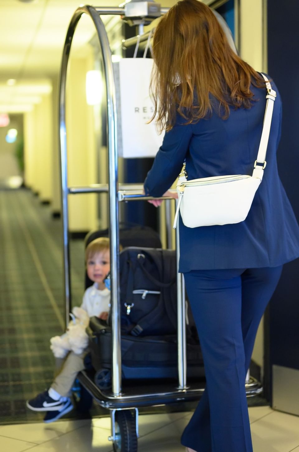 Woman in a blue suit pushing a luggage cart with a toddler sitting among black travel suitcases at Rodd Moncton