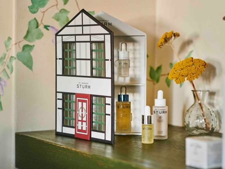 Dr. Barbara Sturm skincare products displayed in a decorative house-shaped box with yellow flowers in a glass vase.