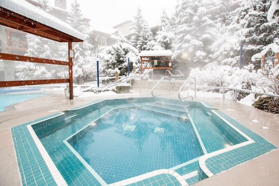 Pool outdoors surrounded by snowy trees at Blackcomb Springs Suites