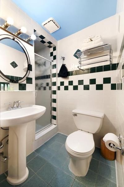 White pedestal sink, white toilet, and shower stall with blue and white checkered walls.