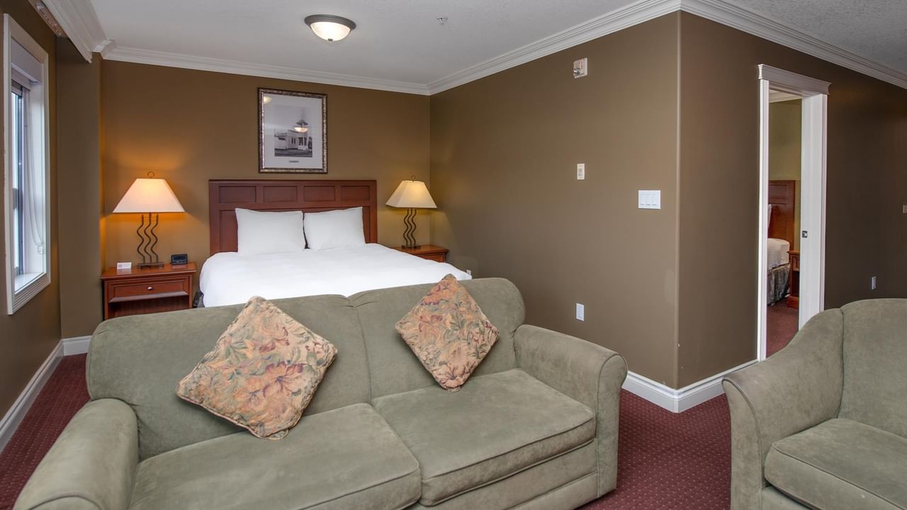 Spacious hotel suite with sage green sofa, white bedding, warm brown walls, and bedside lamps at Coast Edson Hotel.