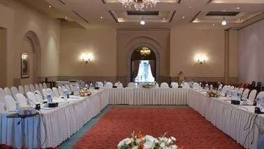 Large U-shaped conference setup with white tablecloths and floral decor under crystal chandelier at Serena Hotels & Resorts