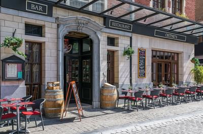Terras met rode stoelen en houten vaten voor een restaurant met bar bij Warwick Brussels Bruxelles