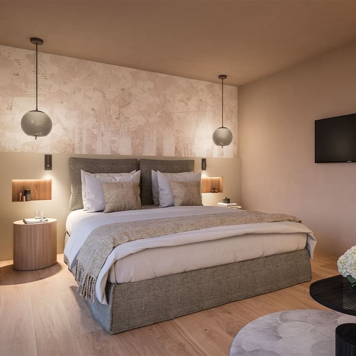 Schlafzimmer mit großem Bett, Wandfernseher, Nachttischen, Hängelampen und Holzboden.