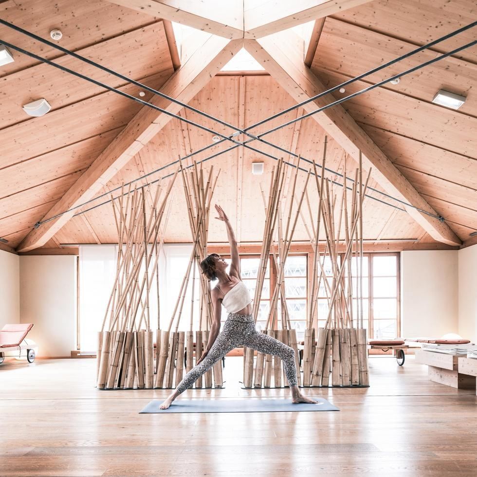 Donna che pratica yoga in una sala con travi in legno e bambù per Club Week ACTIVE.