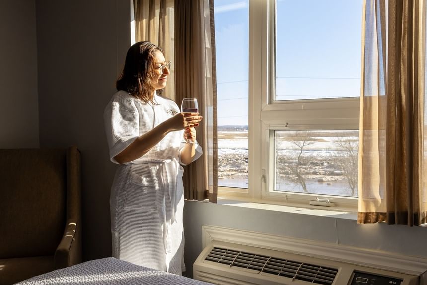 Woman in robe holding glass by window with snowy view in room at Rodd Moncton places to stay in Moncton