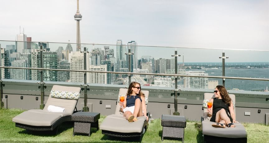 Des femmes se détendent sur la terrasse avec des cocktails et la ville en toile de fond à l'hôtel X Toronto