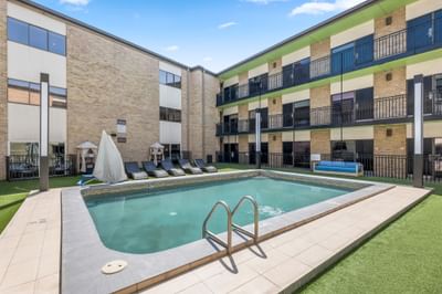 The Riverwalk Plaza Hotel courtyard, with a swimming pool, lounge chairs, shaded cabanas, and multi-story brick buildings