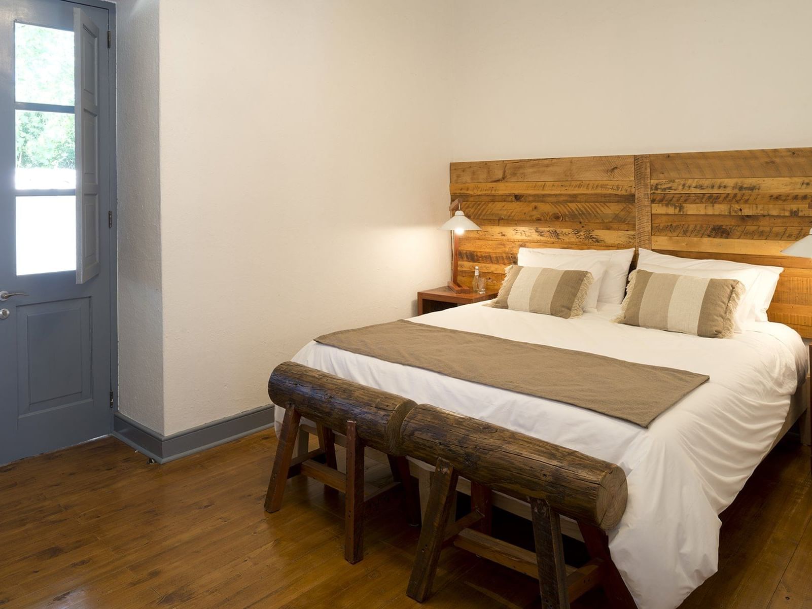 Bancos de madeira junto à cama sob cabeceira de madeira perto de lâmpada na Deluxe King Room do NOI Blend Colchagua