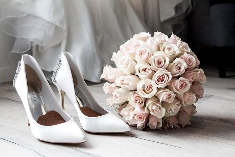 White bridal heels beside a bouquet of pink roses on a light wooden floor at Granduca Houston