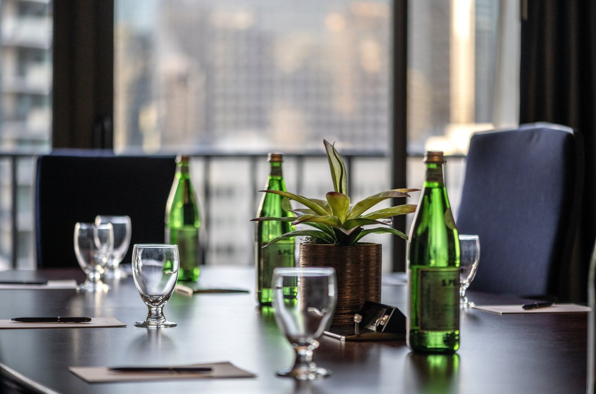 Green water bottles by clear glasses surrounding a potted plant on a table in Boardroom (1808) at Warwick Seattle