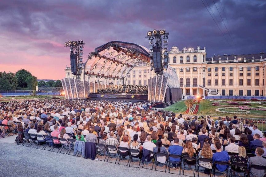 Großes Publikum beim Sommernachtskonzert in Schönbrunn vor historischer Kulisse mit beleuchteter Bühne und klassischer Musik unter freiem Himmel.