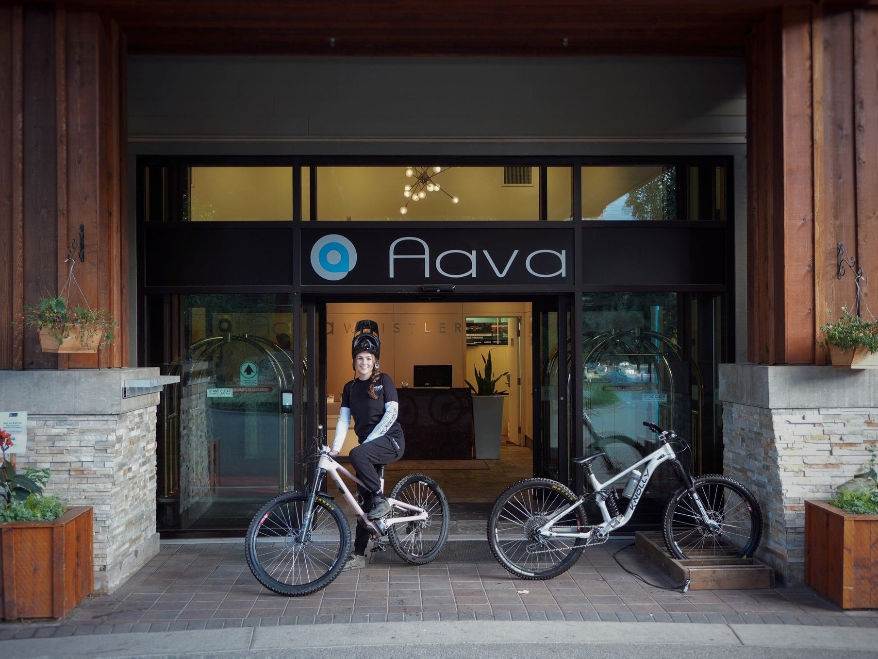 Woman wearing a helmet sitting on a bike in front of Aava Whistler Hotel