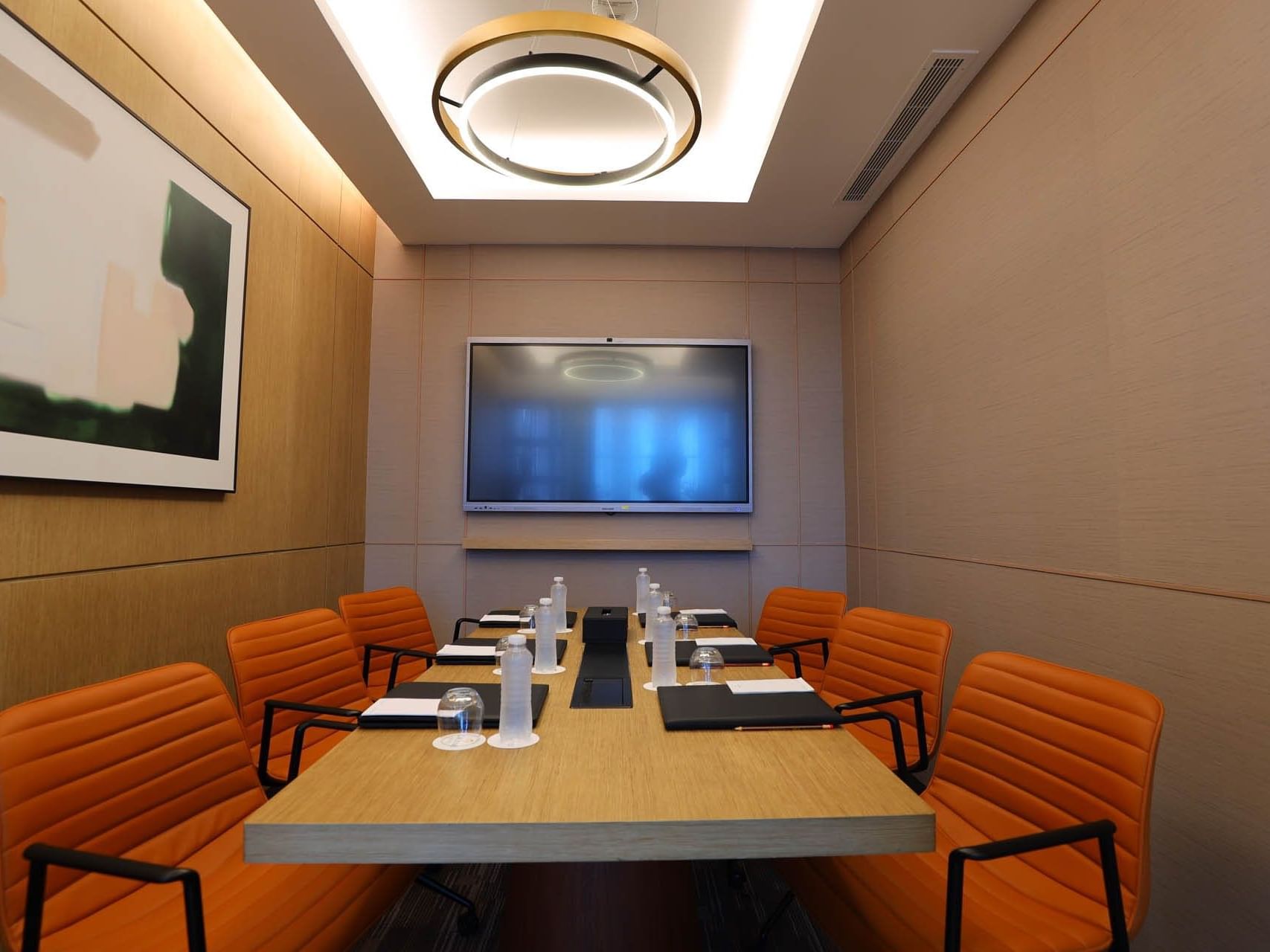 Meeting room with a long table, orange chairs, large monitor, and framed artwork on the wall.