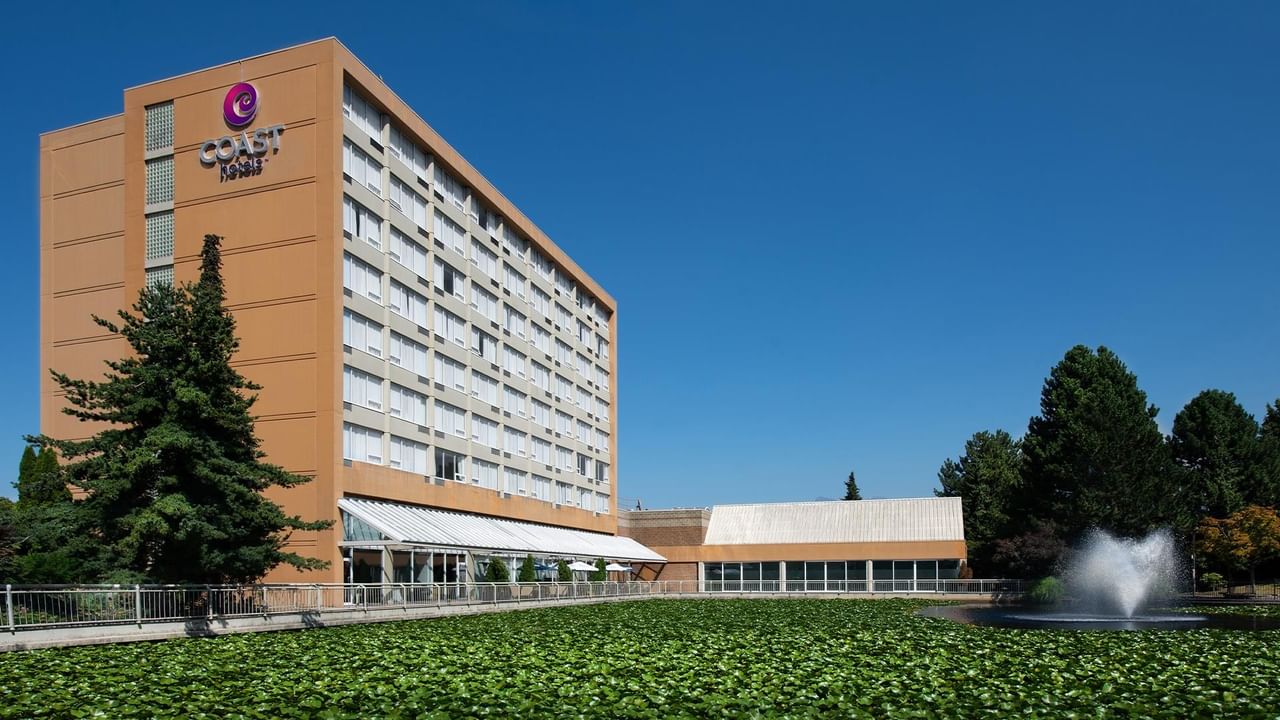Exterior view of Coast Chilliwack Hotel by APA with the hotel tower, lawn and fountain.
