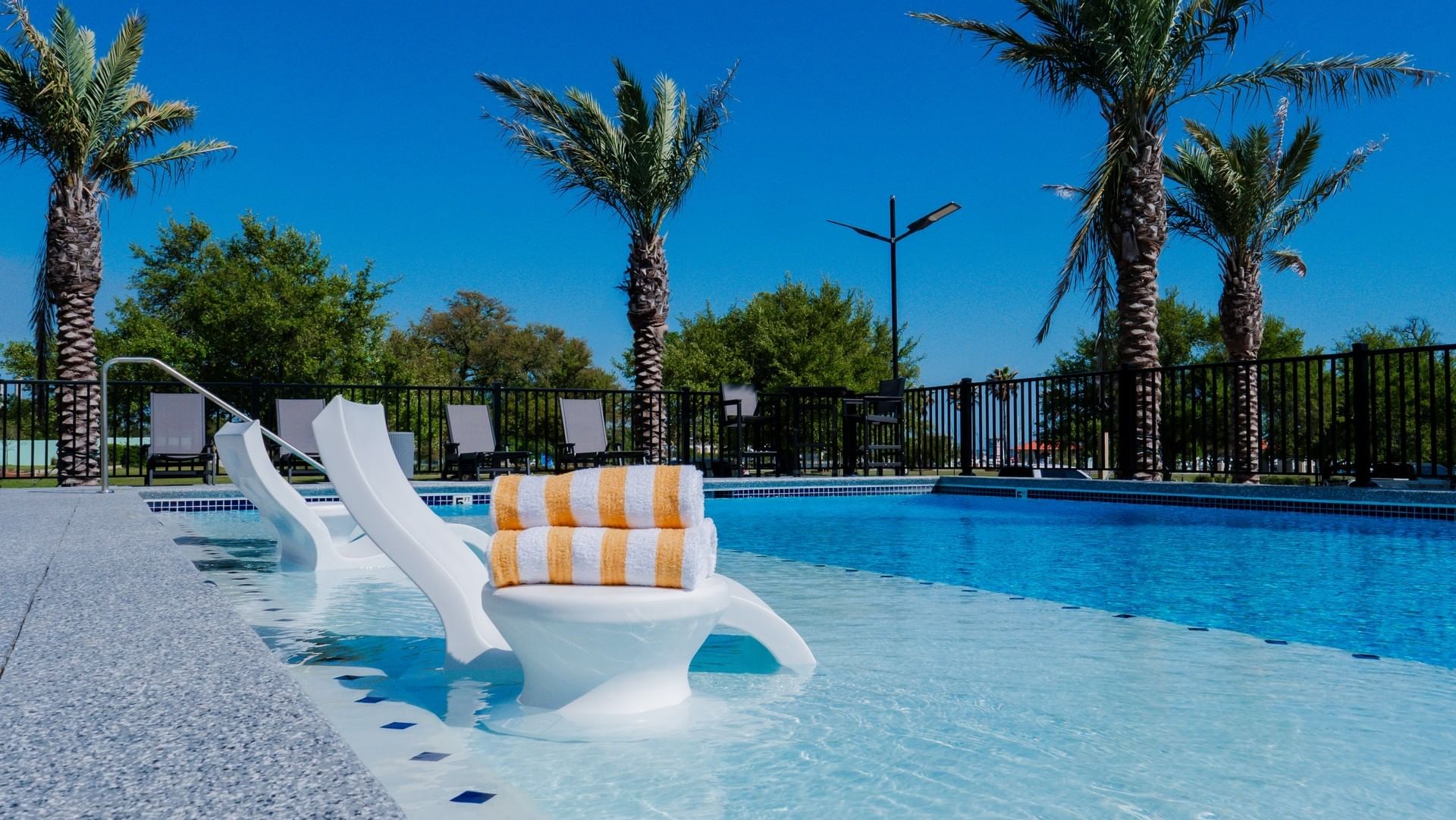 Luxury outdoor pool with white lounge chairs, striped towels, and tropical palm trees at The Markham Hotel