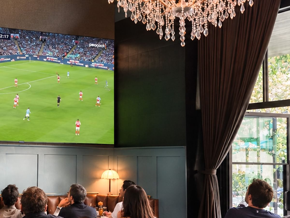 Guests watch a soccer match on a large screen beneath an elegant crystal chandelier during Watch Parties at The Parlor.