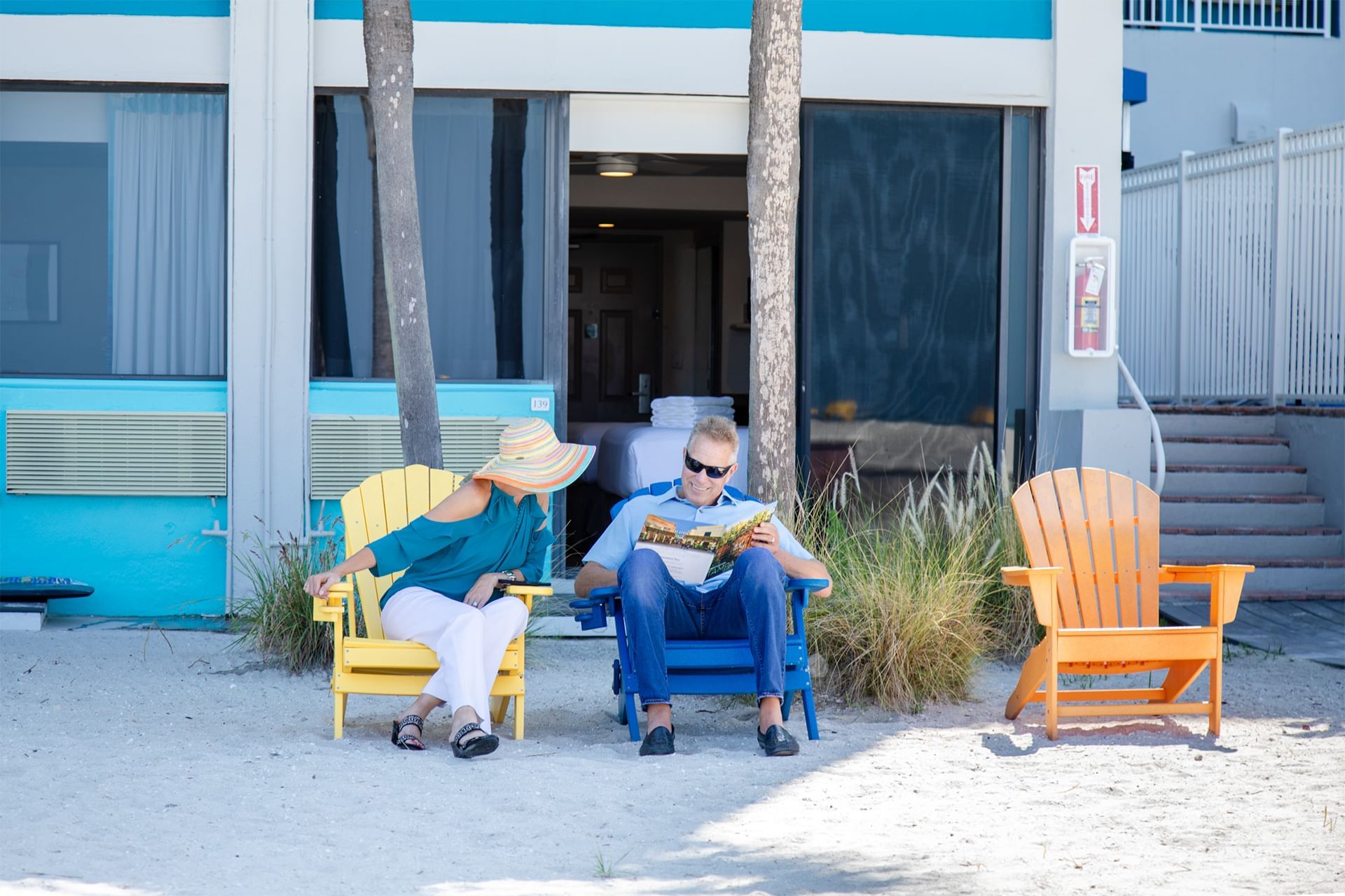 a man and woman sit on the beach and read a magazine