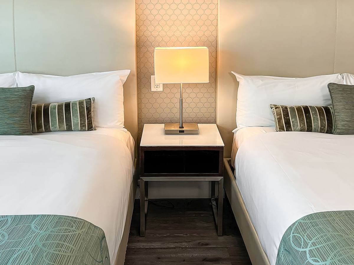 Two beds in hotel room with nightstand and lamp