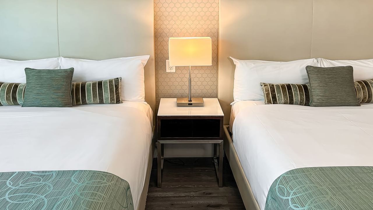 Two beds in hotel room with nightstand and lamp