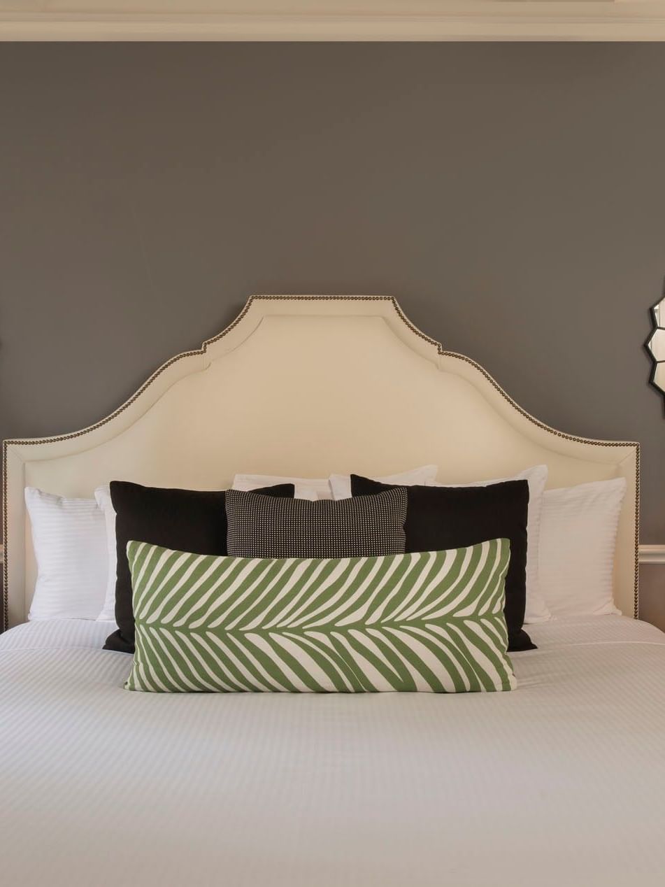 Bed between lamps with green patterned pillows, and sunburst mirrors in Marion Suite at Warwick New York