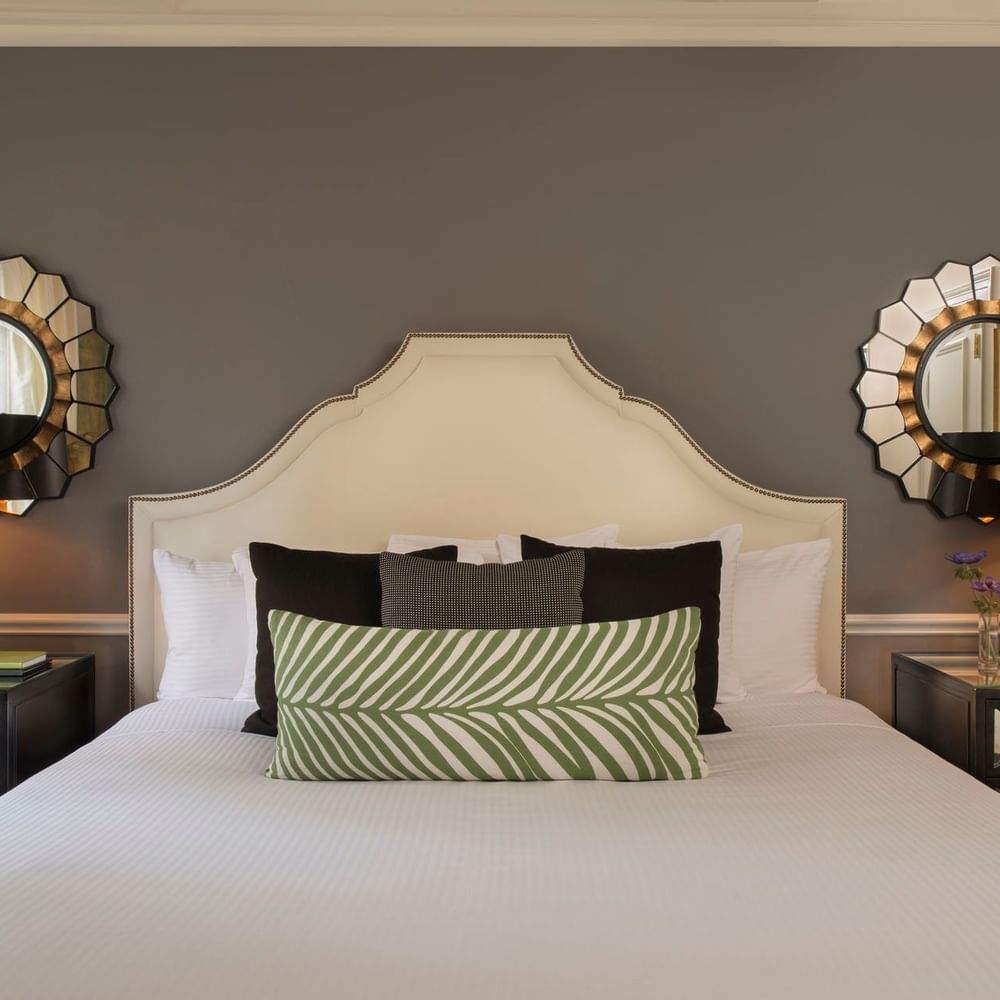 Bed between lamps with green patterned pillows, and sunburst mirrors in Marion Suite at Warwick New York