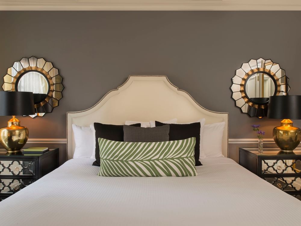 Bed between lamps with green patterned pillows, and sunburst mirrors in Marion Suite at Warwick New York