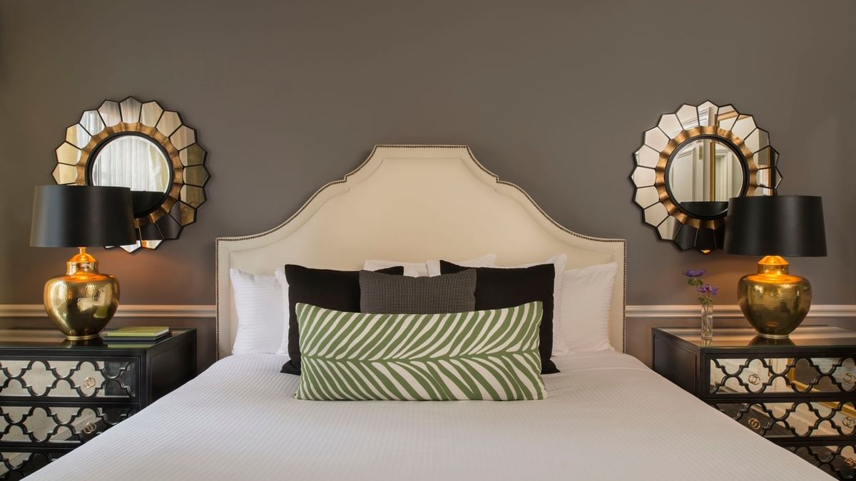 Bed between lamps with green patterned pillows, and sunburst mirrors in Marion Suite at Warwick New York
