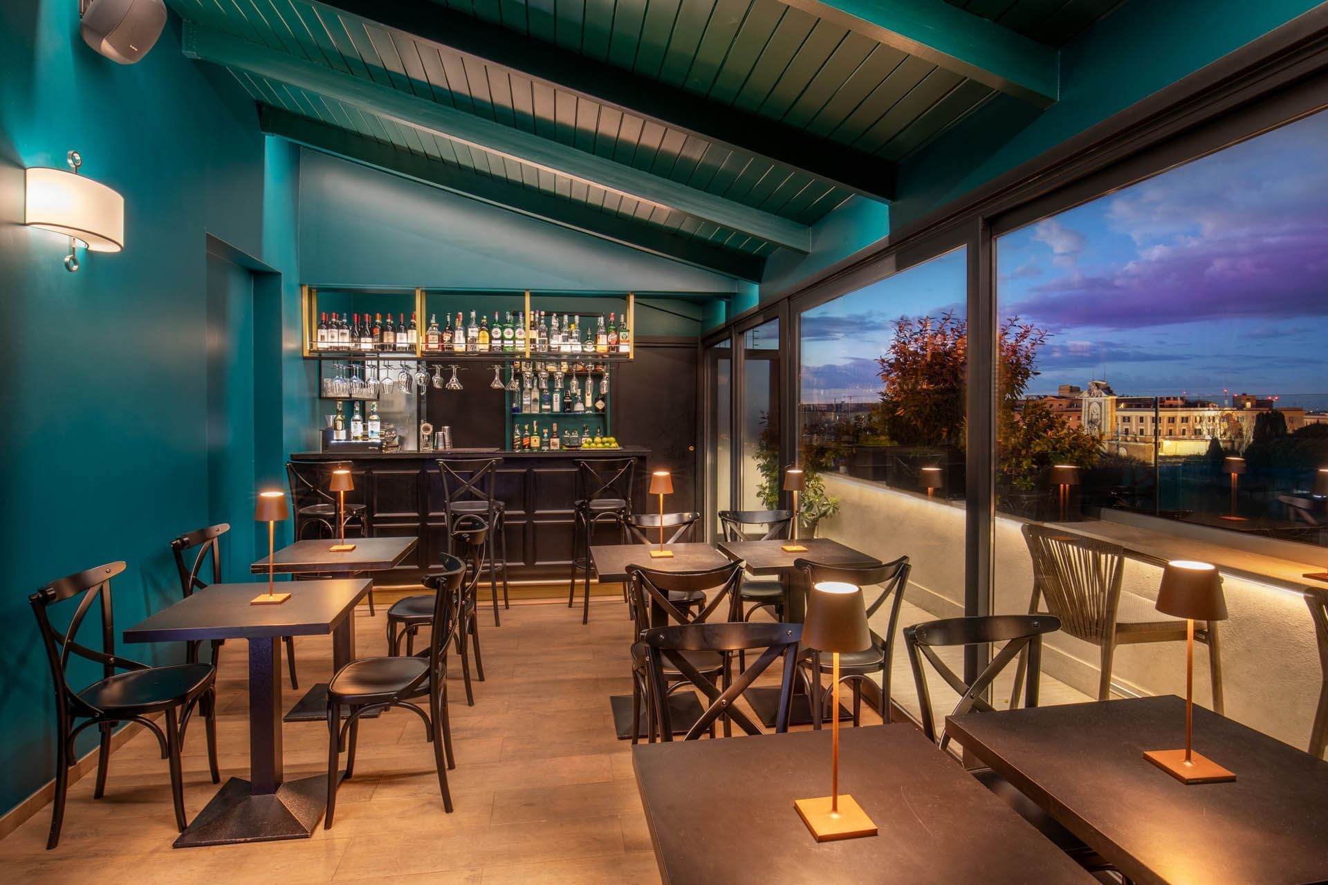 Terrazza Costanza bar at The Guardian Hotel with teal walls, elegant tables, a shelf, and large windows with a scenic view