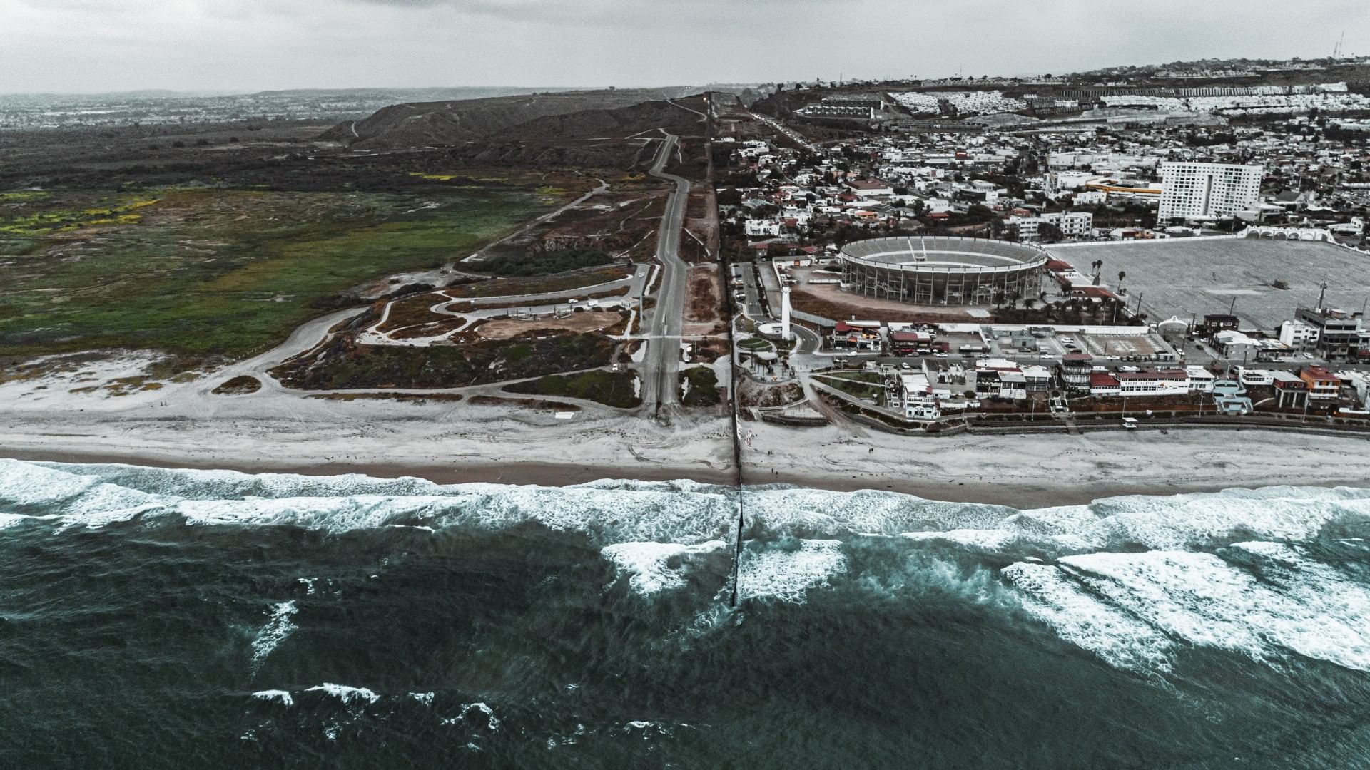 Aerial view of the San Diego coastal border fence dividing two distinct landscapes near the Real Inn Tijuana