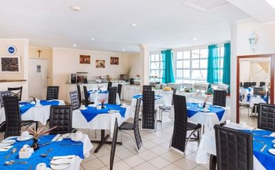 Bright dining area with white and blue tables set for breakfast, featuring chairs, and dishes at Bay Gardens Inn